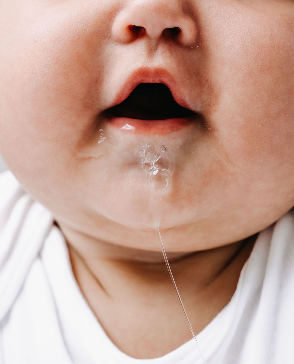 Close-up of a baby's mouth with drool or milk droplet.