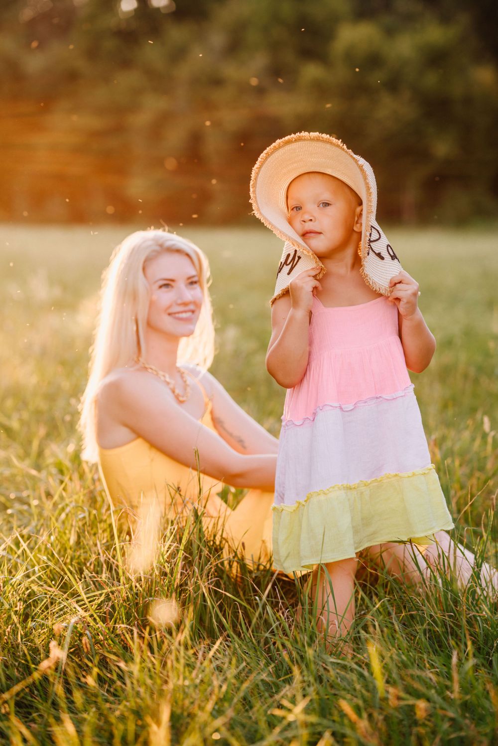Children in summer dresses sitting together on grass during golden hour.