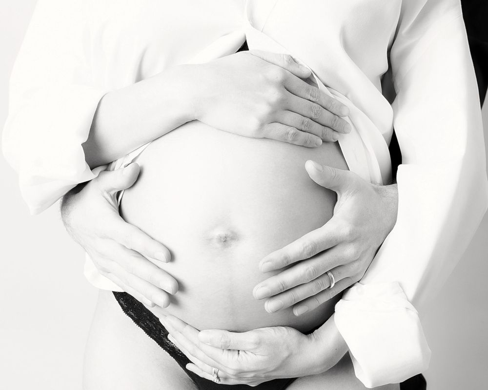 Black and white artistic photograph of hands around a pregnant belly.