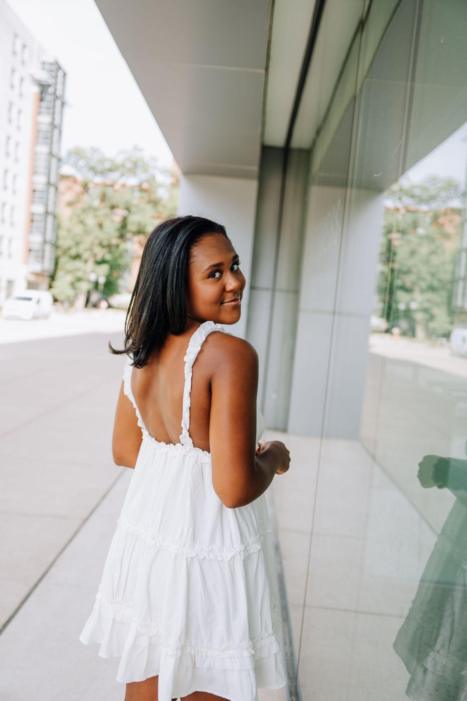 Person in flowing white summer dress poses gracefully in outdoor corridor.