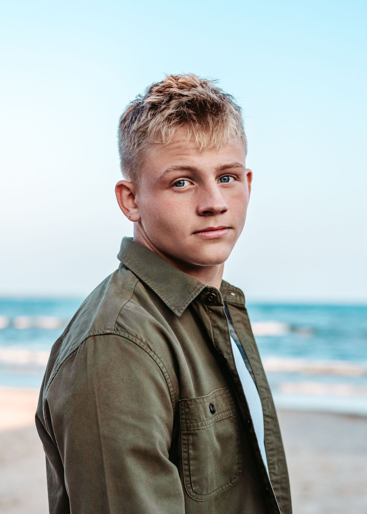 Portrait of young person in olive jacket against ocean background.