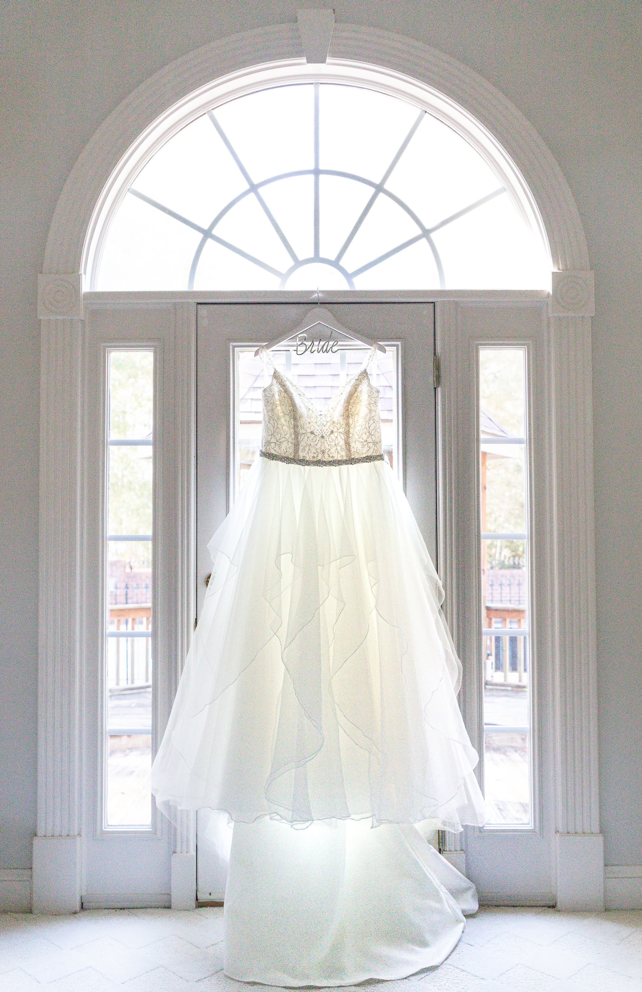 The bride's exquisite wedding dress hanging in a dreamy setting, evoking a sense of anticipation and bridal elegance.