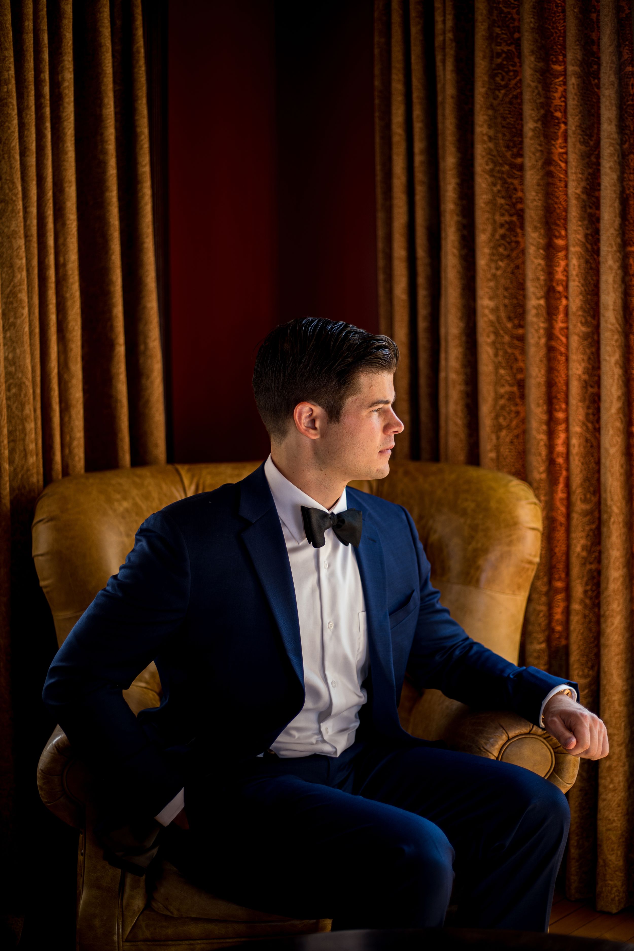 The groom seated in a leather chair, exuding a sense of refinement and relaxation before his special day.