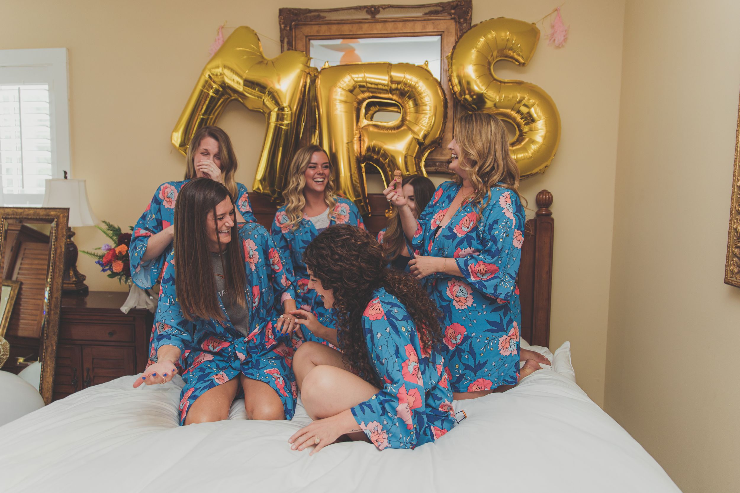 Bridesmaids in coordinating pajamas gathered on a bed, radiating joy and camaraderie, sharing pre-wedding excitement