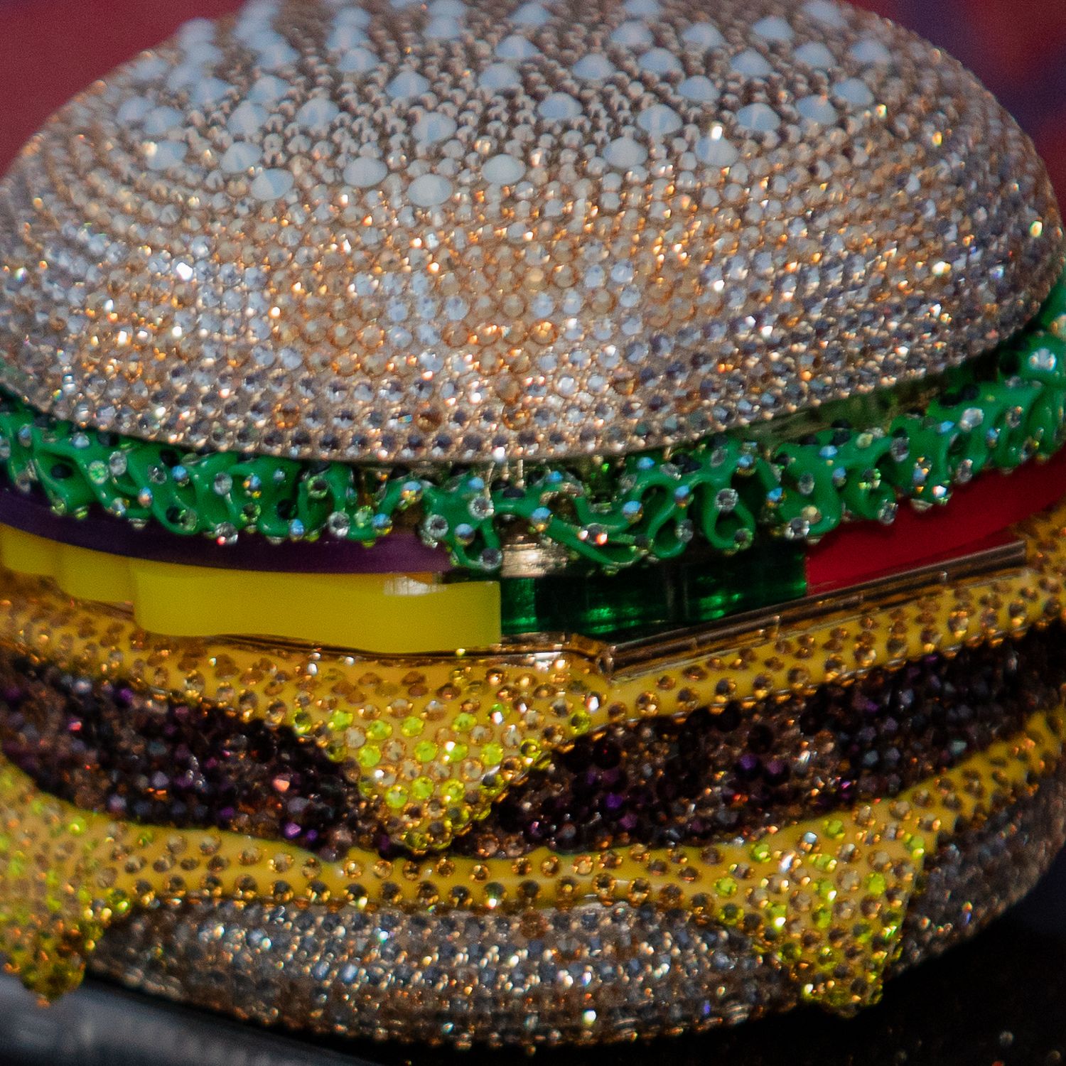 A crystal-encrusted hamburger sculpture sparkles with colorful rhinestones in green, yellow, and brown tones.