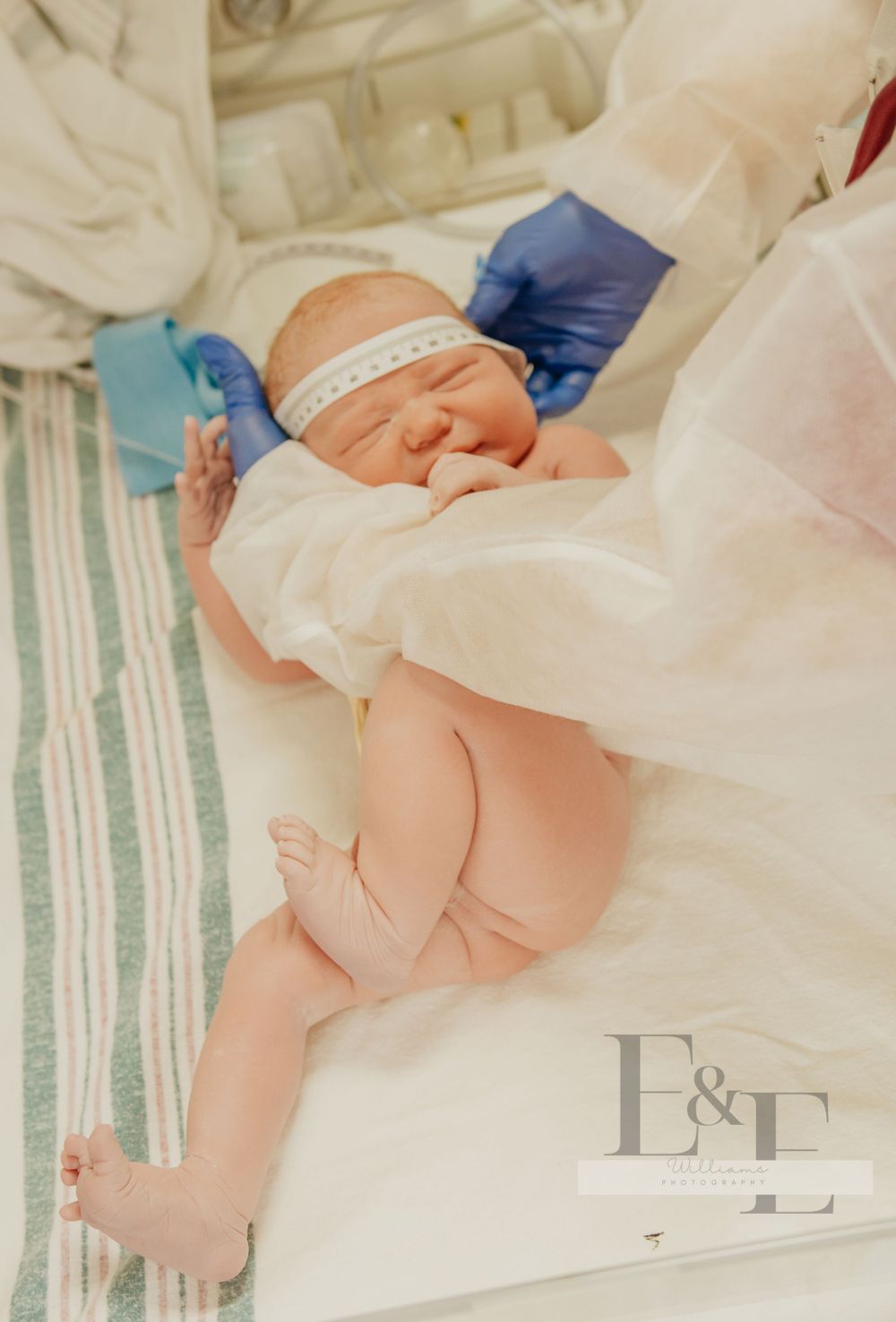 Newborn baby wrapped in white hospital blankets receiving medical care.