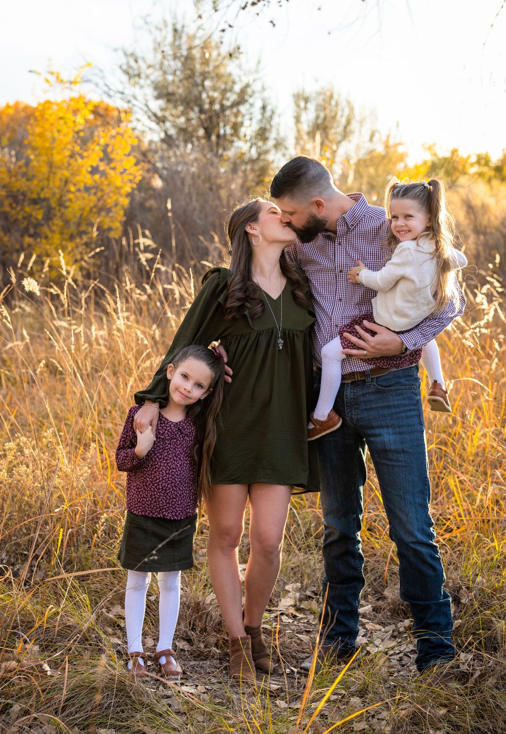 A family shares an intimate moment together in a golden field at sunset.