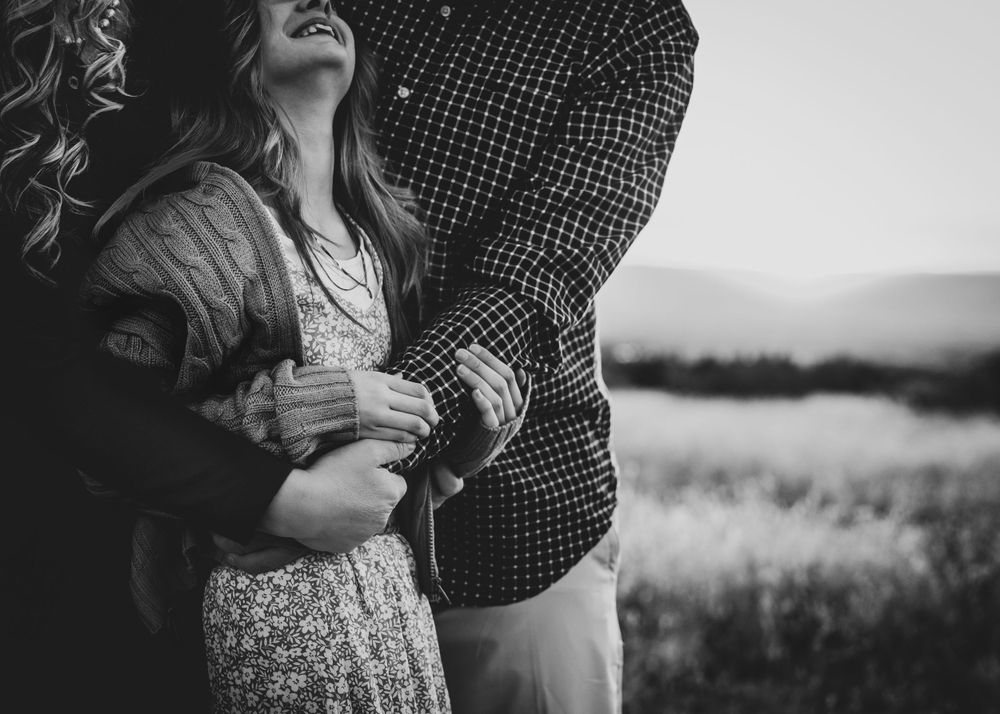 A couple embraces and laughs together in a black and white portrait outdoors.