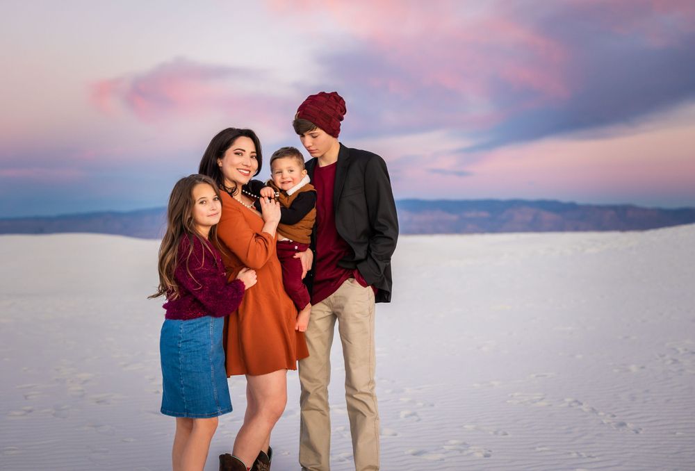 Family group wearing warm colors poses together on white sand at sunset.