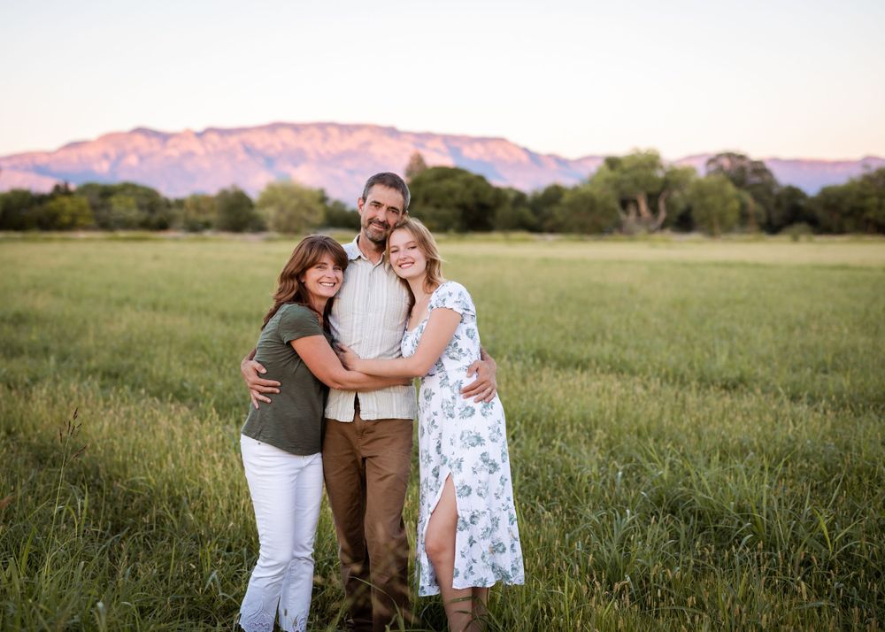A loving family group hug against a backdrop of pink mountains at sunset.