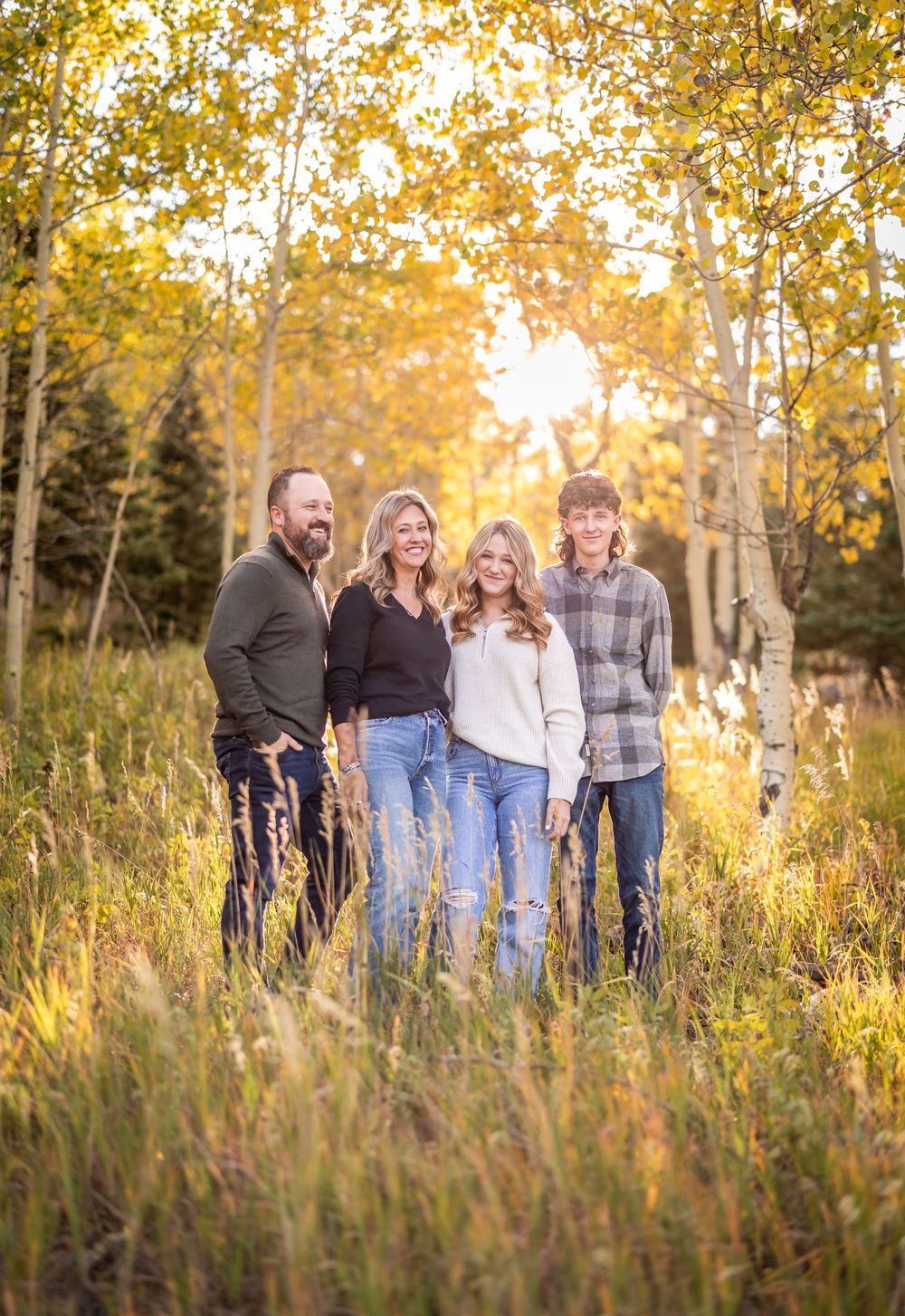 A family portrait of four people standing among fall aspens in golden evening light.