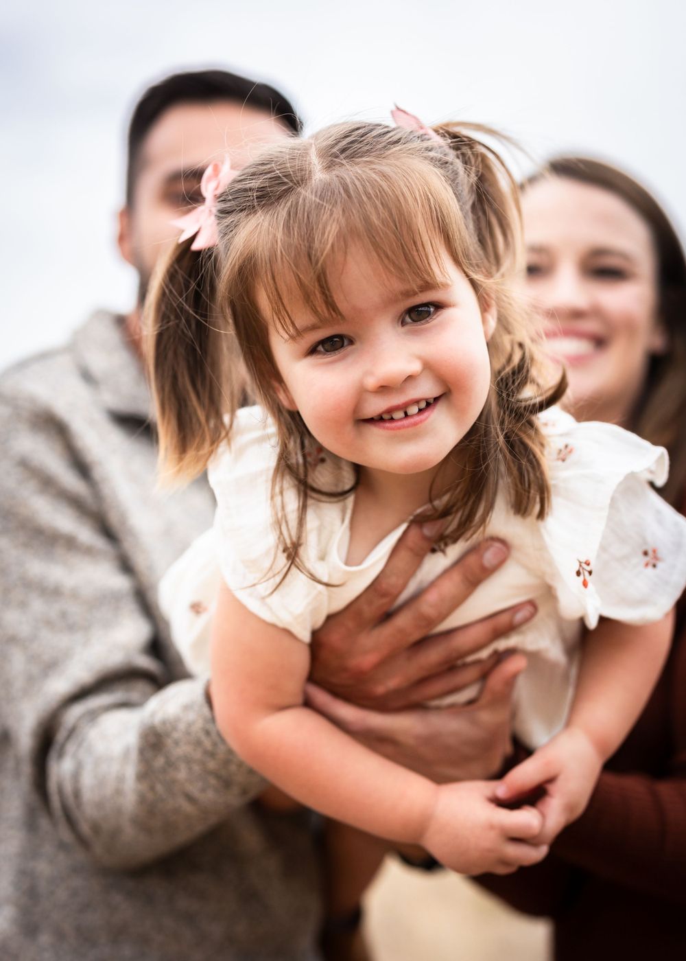 A happy toddler with pigtails smiles while being held in a candid family photo.