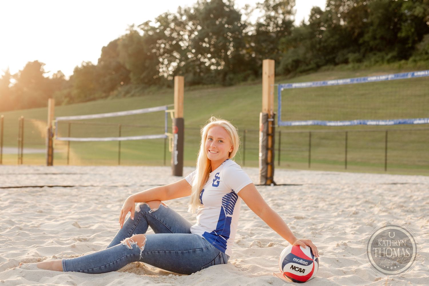 Volleyball player relaxes on sandy court during golden hour sunset with sports equipment.