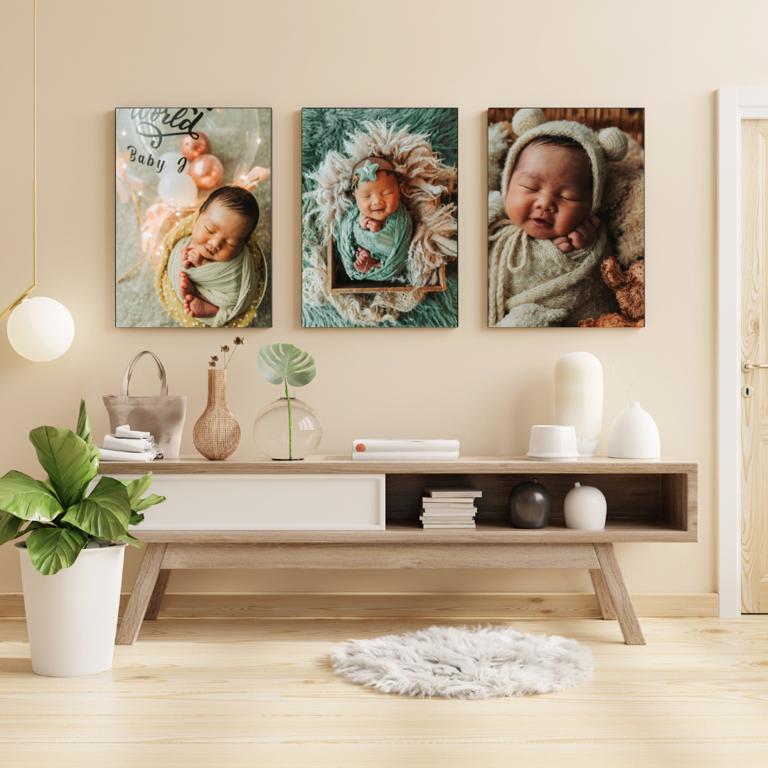 Three newborn baby portrait canvases displayed on a wall above a wooden sideboard in a modern living room.