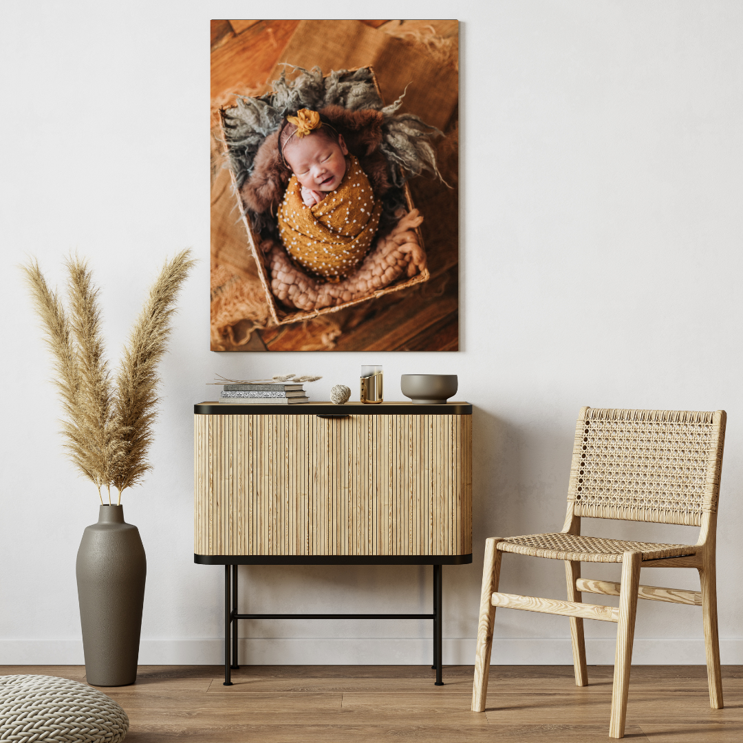Canvas print of a smiling newborn wrapped in yellow, displayed on a wall above a wooden sideboard in a cozy room.