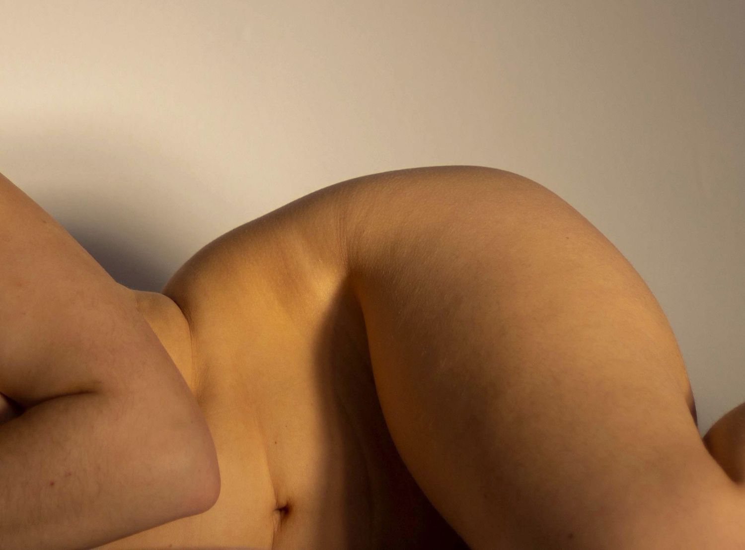 Close-up artistic photograph of human body curves and skin texture against a neutral background.