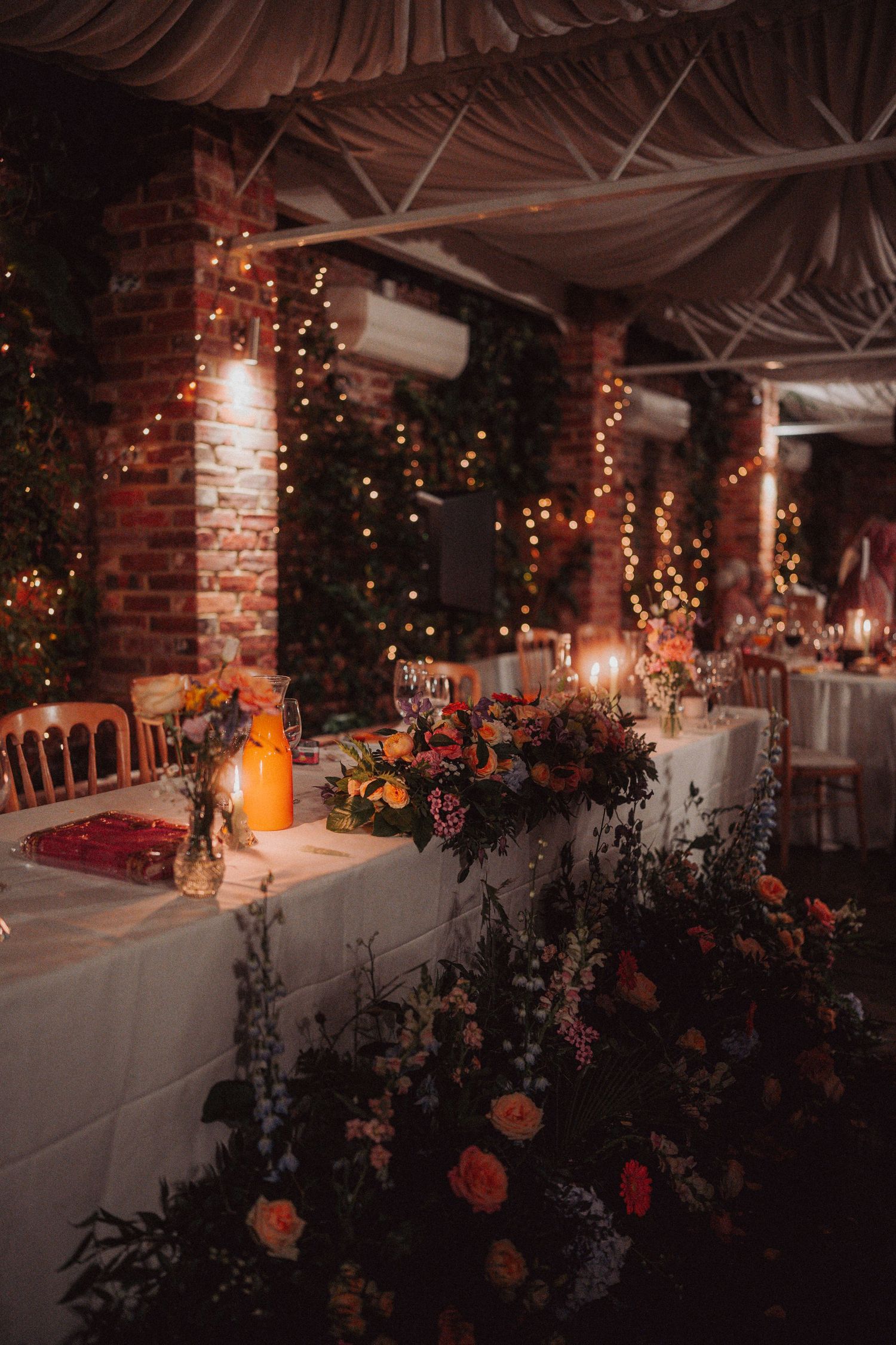 An intimate wedding reception setup with floral arrangements and twinkling lights in a rustic brick venue.
