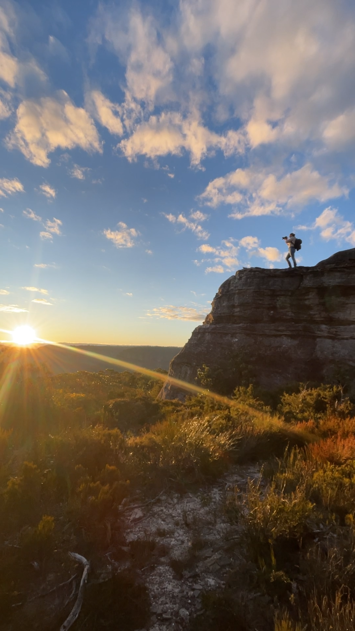 Photographer on a mountain in the blue mountains, taking photos at sunset.