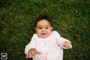 A small child lying on grass smiles joyfully at the camera.