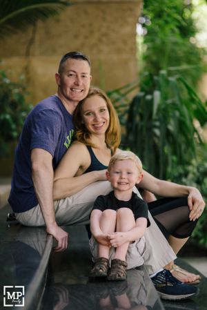 A family sits together on a stone ledge with greenery in the background on a sunny day.