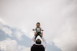 A child is lifted high in the air against a cloudy sky background.