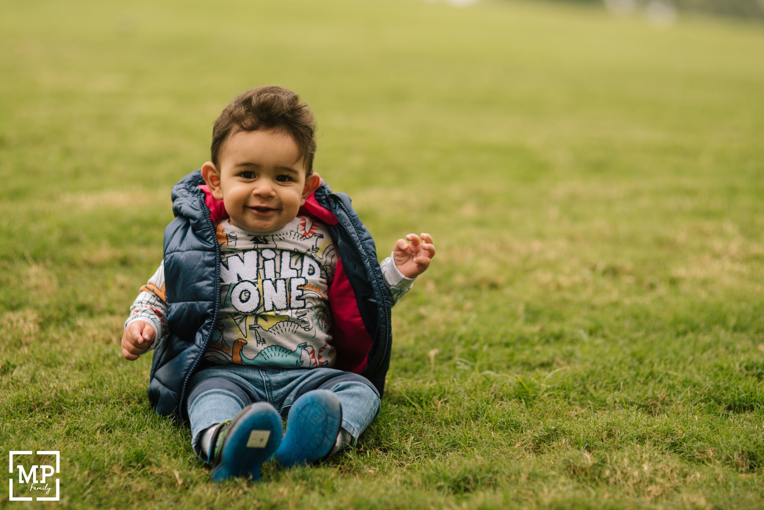 Toddler sitting on grass wearing wild one shirt and denim jacket.