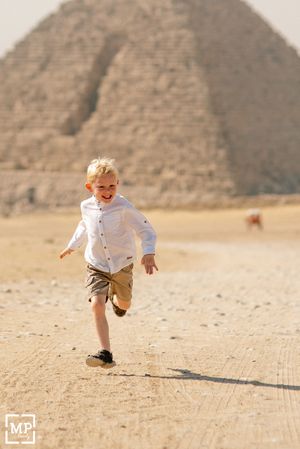 Young child runs excitedly across desert sand with an ancient Egyptian pyramid in the background.