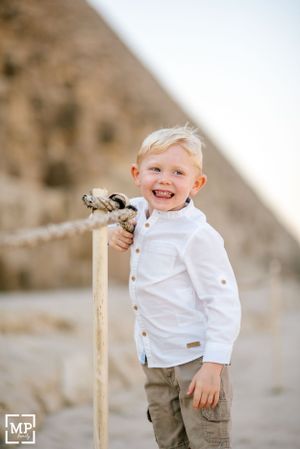 A young child in white shirt smiles while holding a walking stick near ancient pyramids.