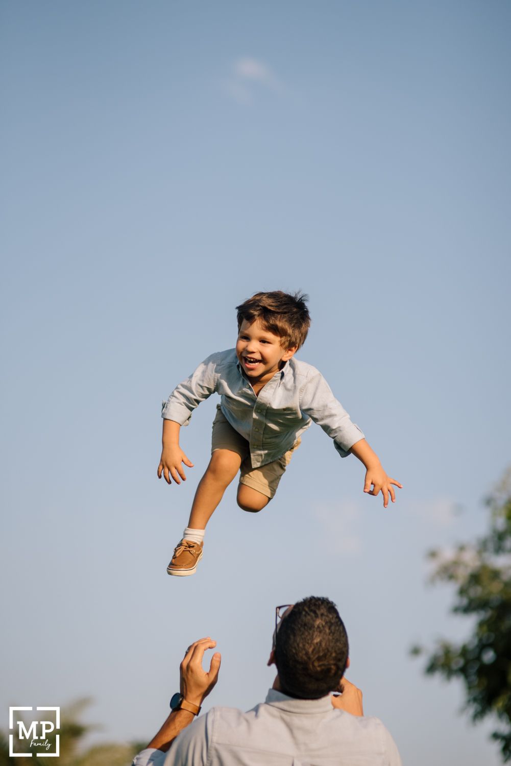 Parent tossing child high in air against blue sky during playful moment.