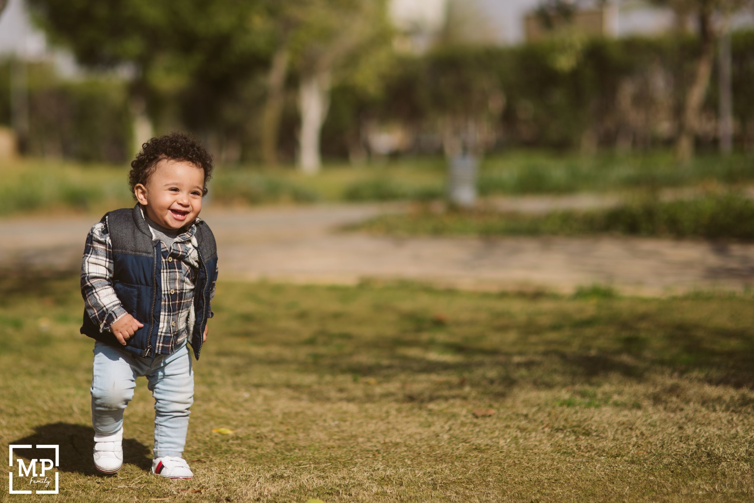 Small child laughs while walking on grass in a park setting.