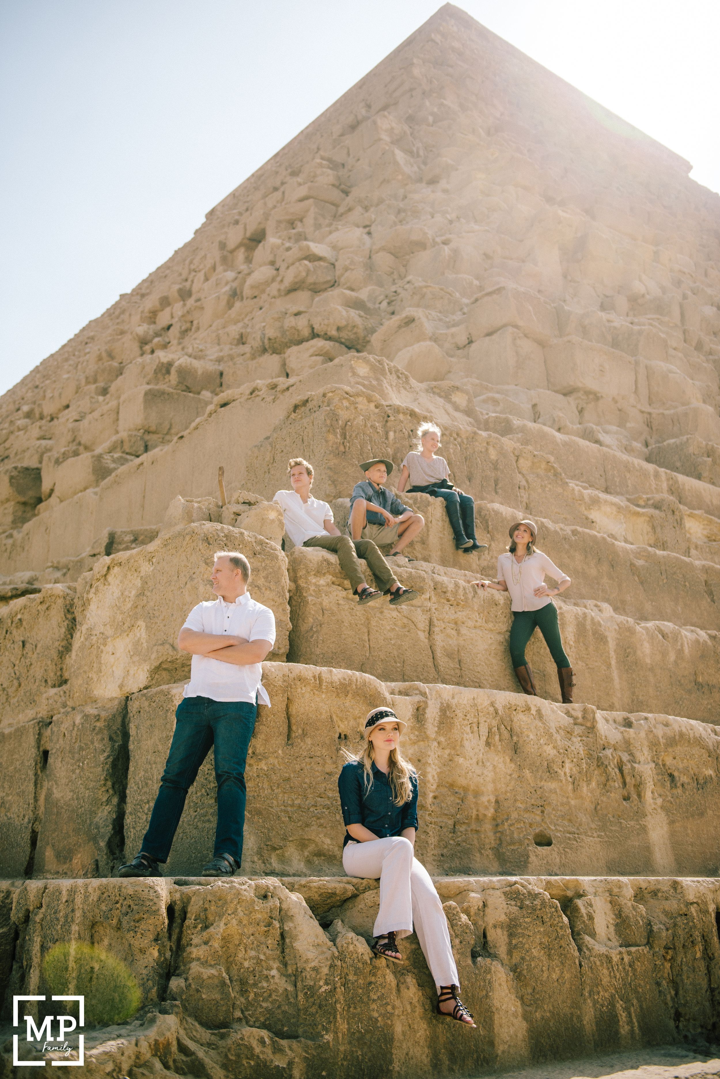 Group poses on ancient Egyptian pyramid stones during sightseeing tour.