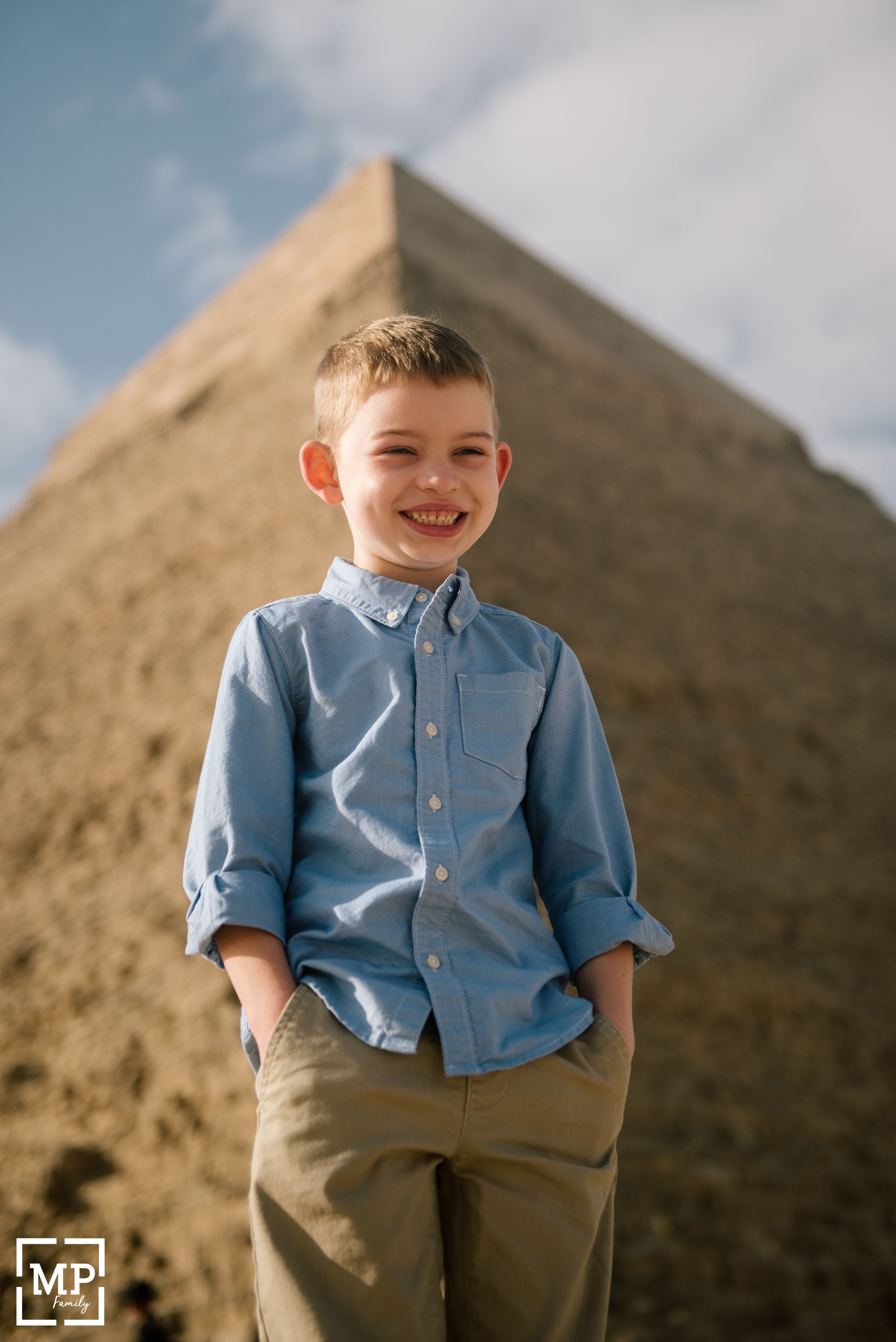 Child stands confidently against the backdrop of a massive Egyptian pyramid under blue skies.