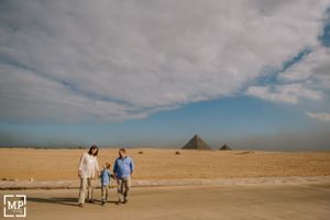 Family walks together across desert sands with pyramids visible in the distance.
