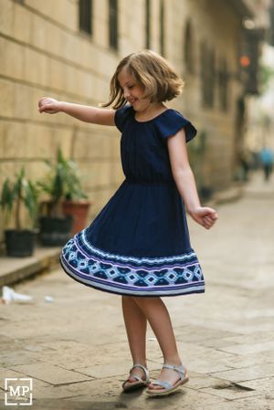 Young girl in navy blue dress twirling on a cobblestone street.