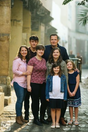 Family group portrait on cobblestone street with historic architecture in background.