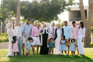 Large family portrait outdoors in coordinated white and pastel outfits on a sunny day.