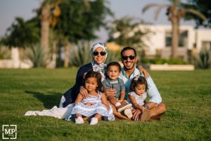 Family group sitting together on grass with palm trees in background wearing coordinated outfits.