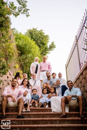 Large family group in coordinated pink and white outfits posed on outdoor stone steps.