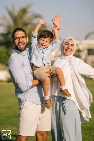 Family of three celebrating joyfully together on a grassy lawn with palm trees in background.