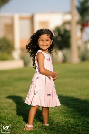 Young child in pink patterned dress smiling while standing on grass.