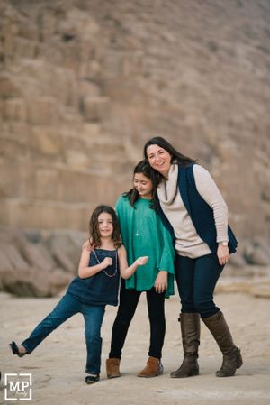 Three people in casual wear share a playful moment against a stone wall backdrop.
