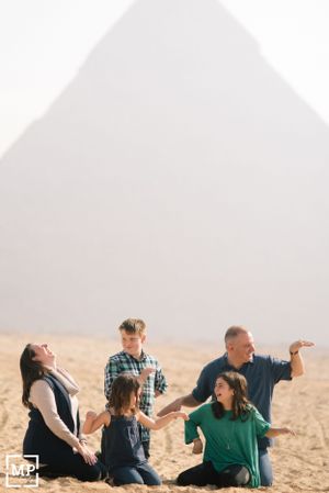 Family group sitting and laughing together in front of a pyramid in the desert.