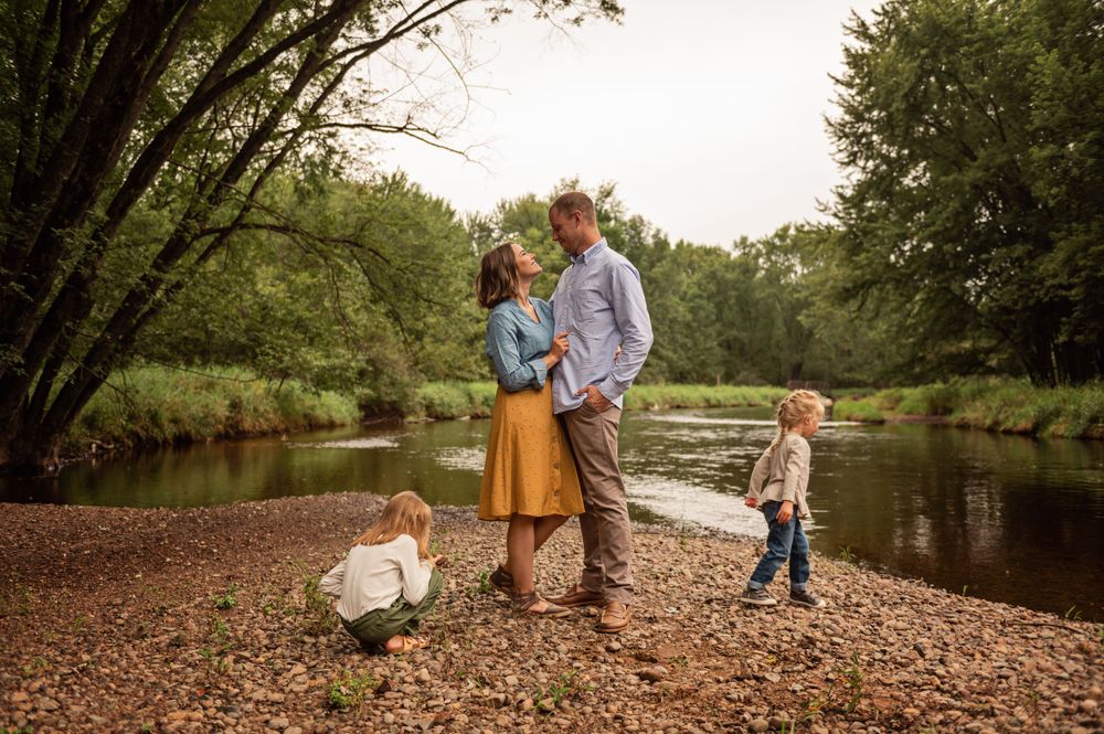 A family enjoys a peaceful afternoon by a river with their dog in a scenic wooded setting.