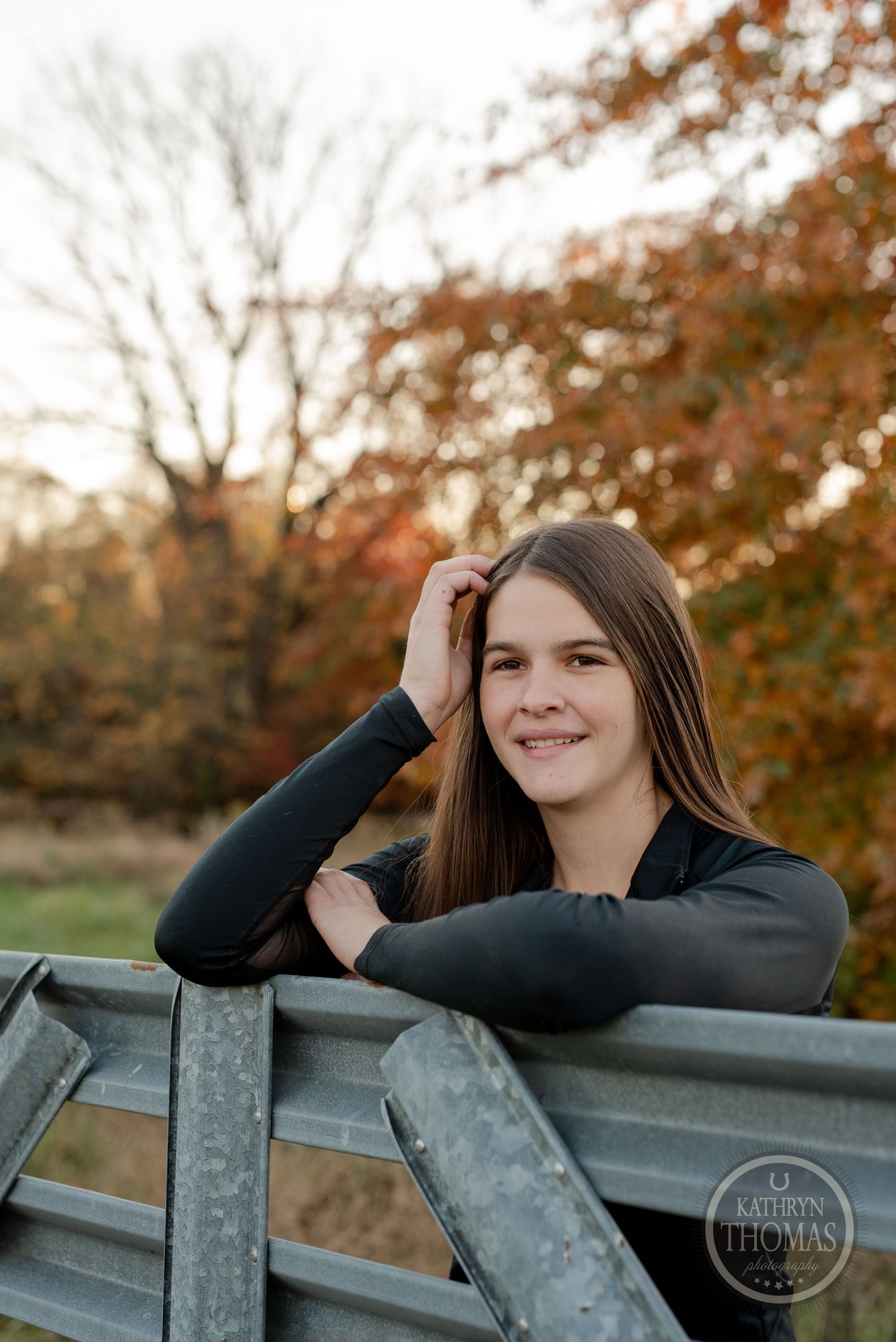 Autumn portrait by metal fence with golden sunset lighting and fall foliage.