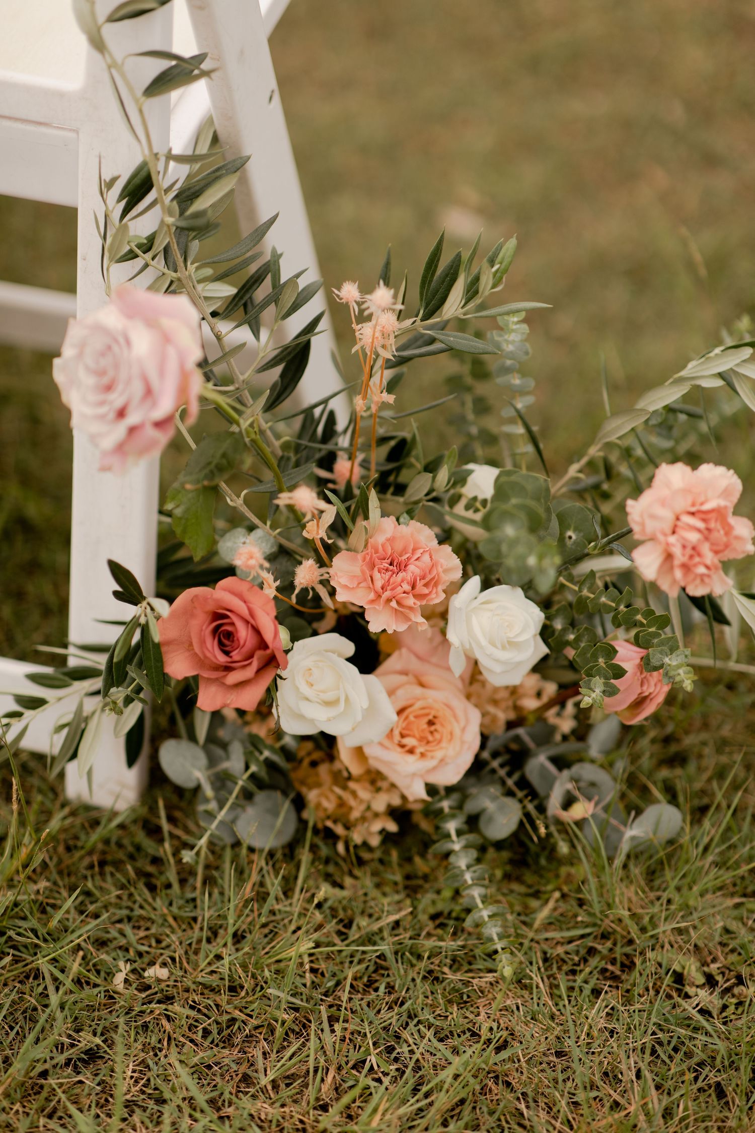 Romantic floral arrangement with coral and white roses decorating a white ceremony chair.