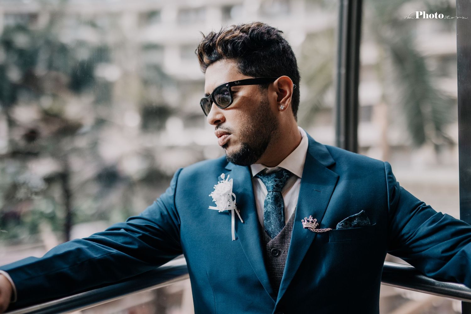 Stylish figure in blue suit and sunglasses poses against an outdoor backdrop.