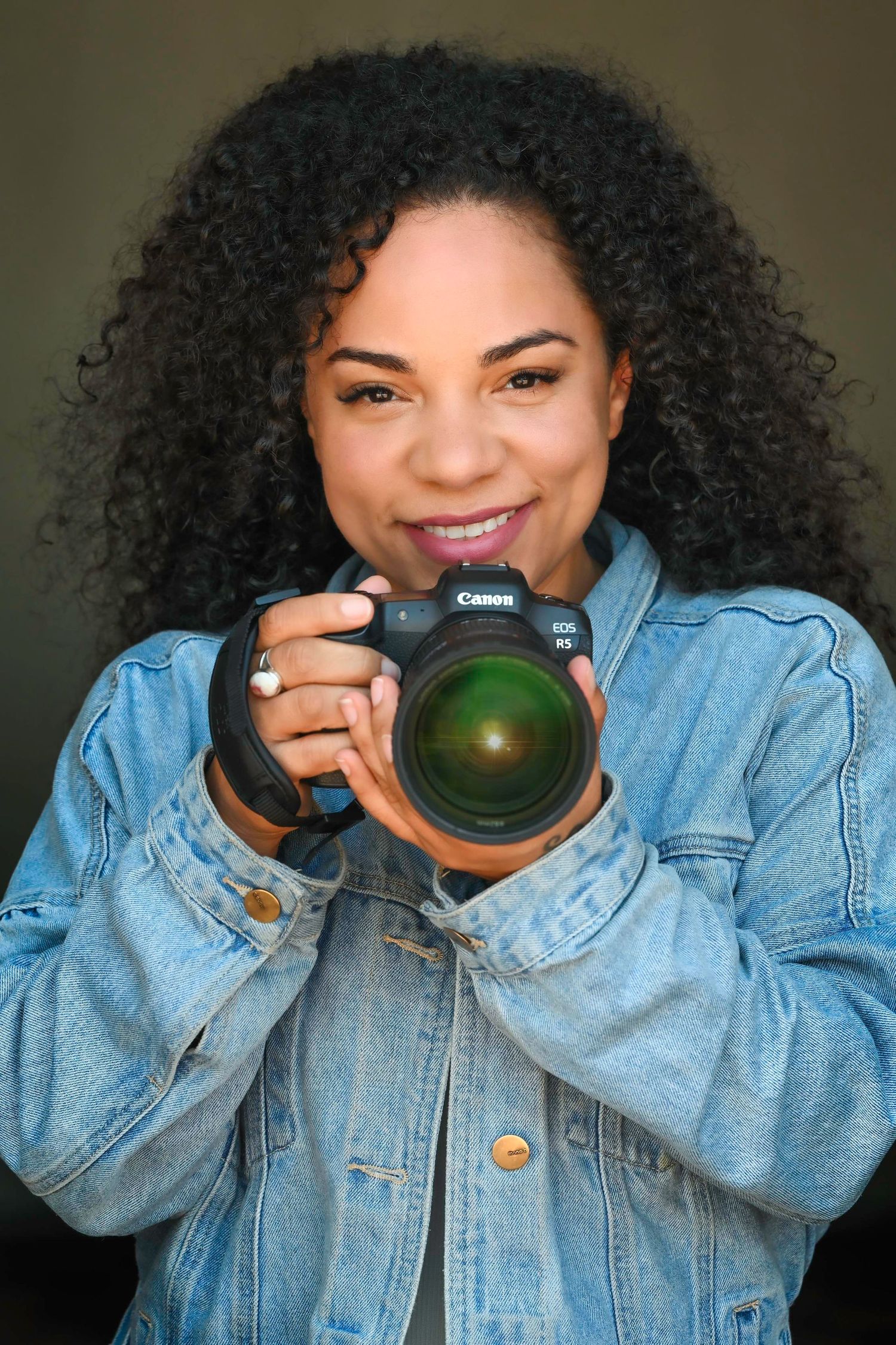 Photographer in denim jacket using Canon camera with wide angle lens against dark background.
