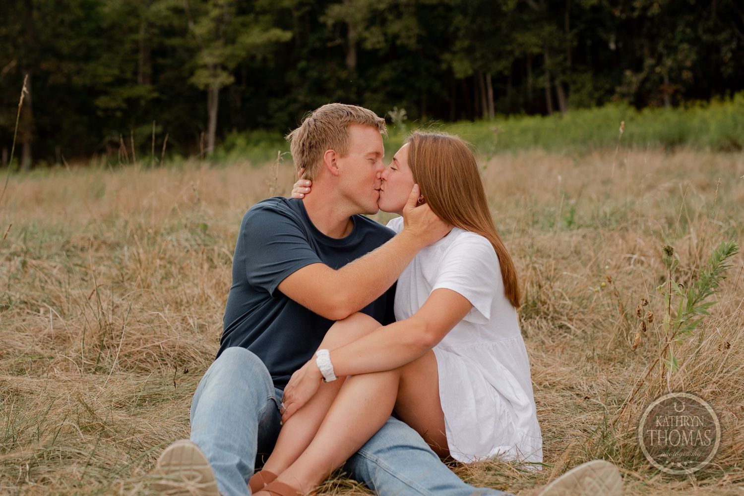 An intimate moment between a couple sitting in a sunlit field.