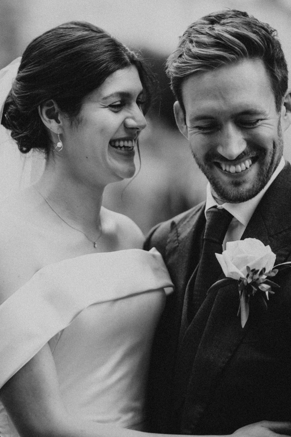Candid black and white portrait of a joyful bride and groom sharing a laugh.