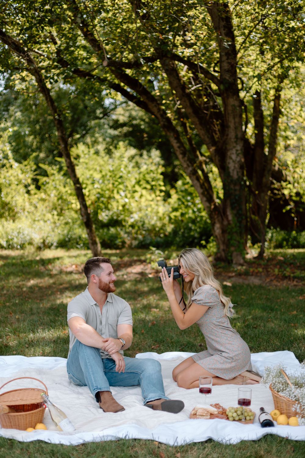 Couple enjoys picnic in park as woman takes photos of partner.